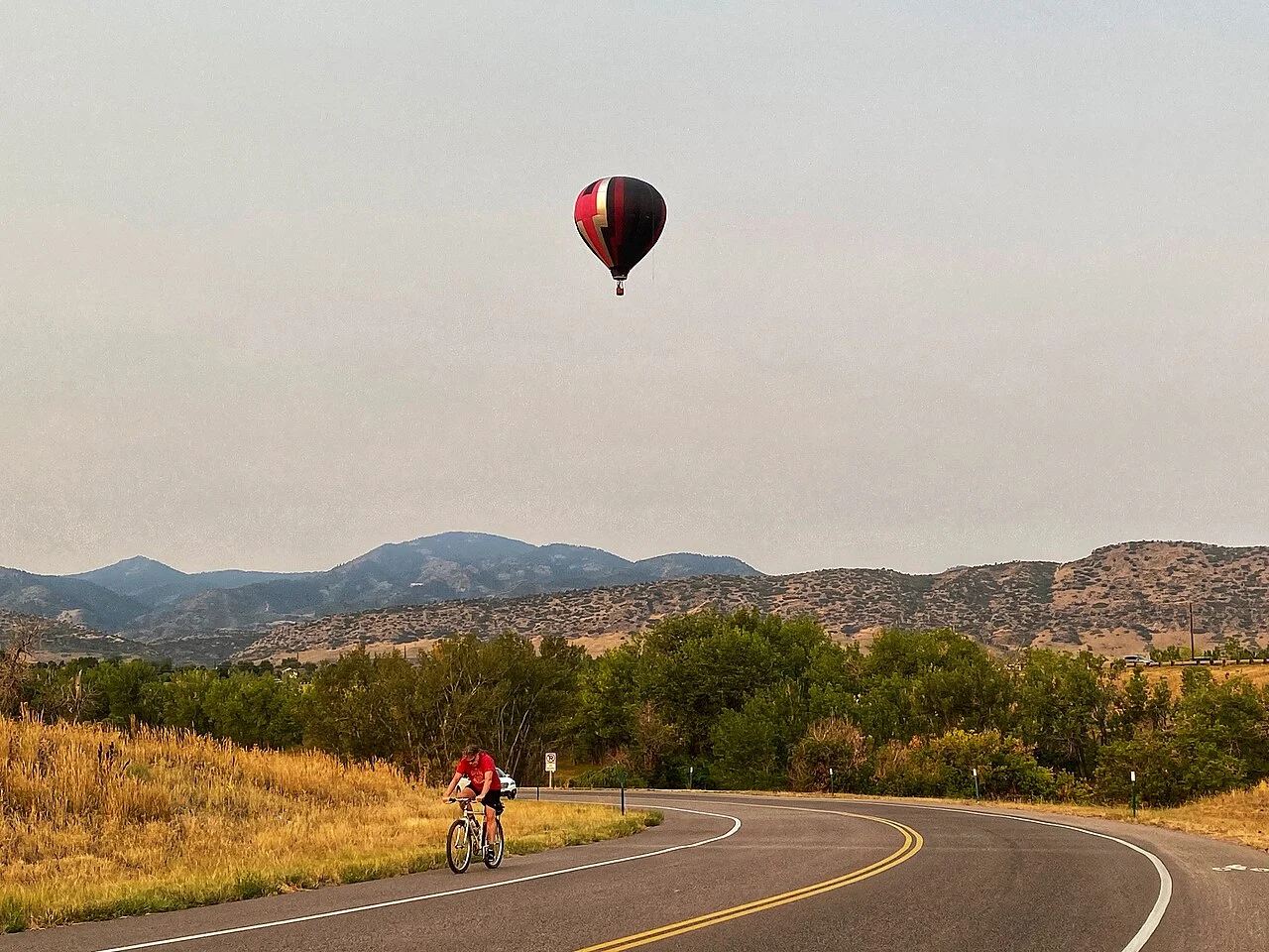 A cyclist beside Chatfield Reservoir with a hot-air balloon above the water.