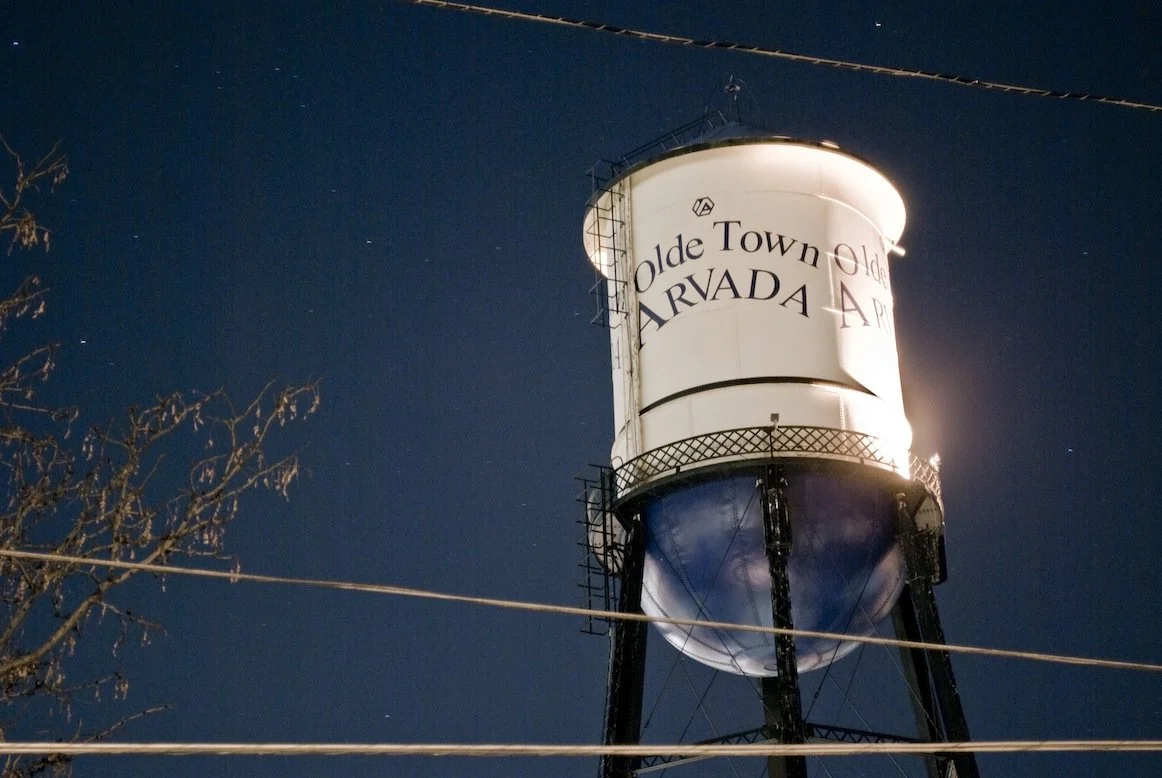 The illuminated Olde Town Arvada water tower at night.