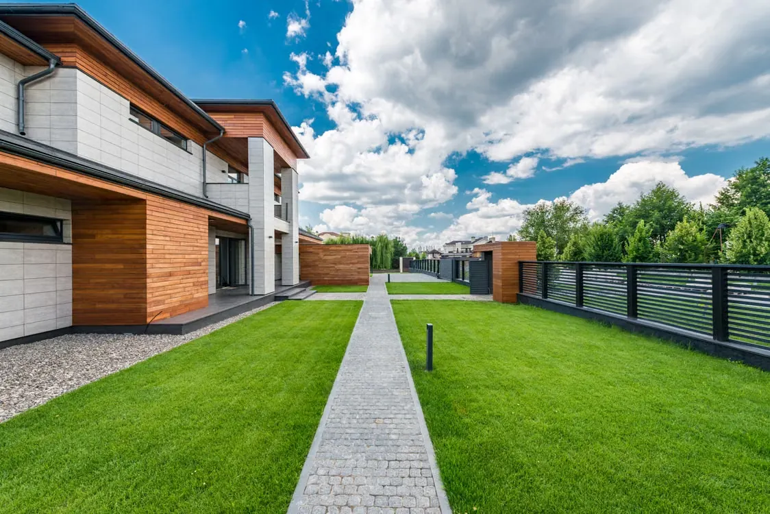 Modern home with a long lawn and white fence.