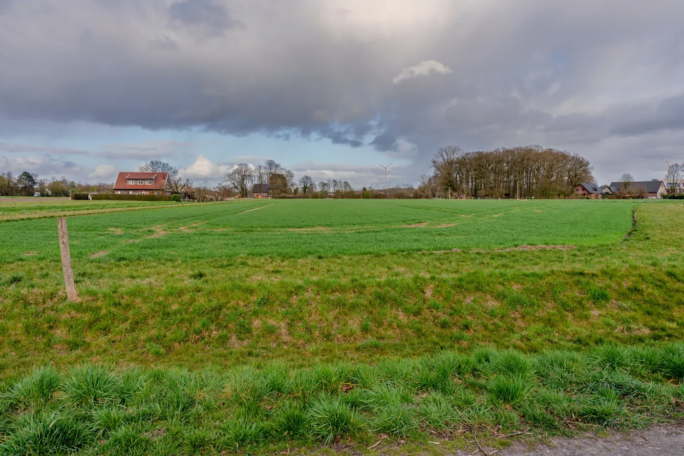 Farmhouse beside broad green fields in a rural landscape