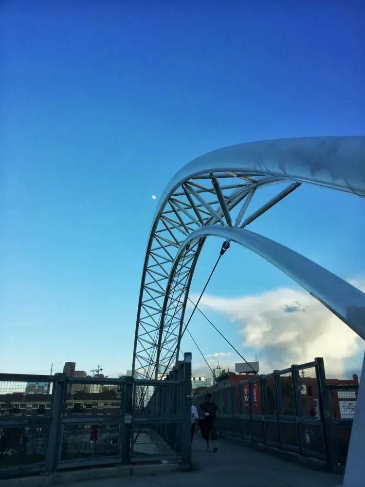 Curving Highland pedestrian bridge beneath a blue Denver sky