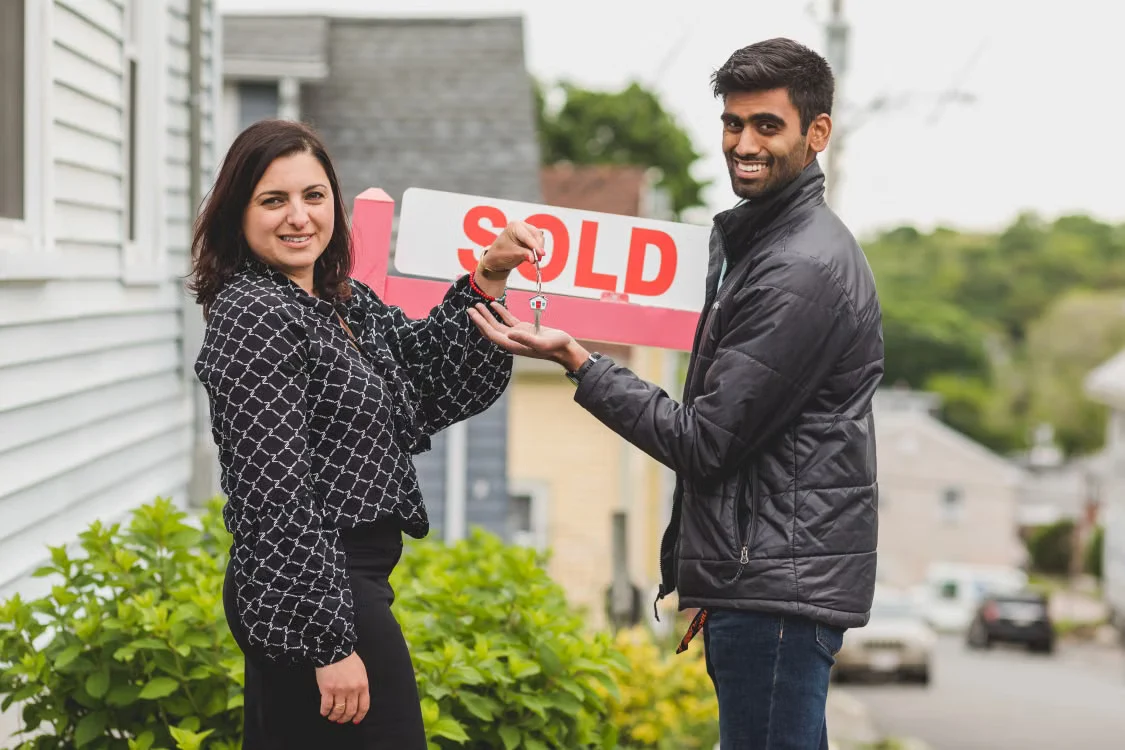 A couple holding their new house key beside a sold sign.