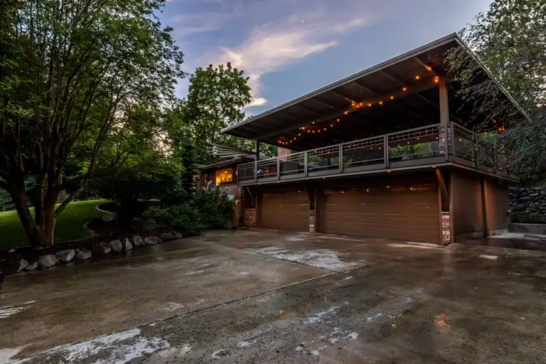 Contemporary house at twilight with warm string lights, a broad balcony and mature landscaping